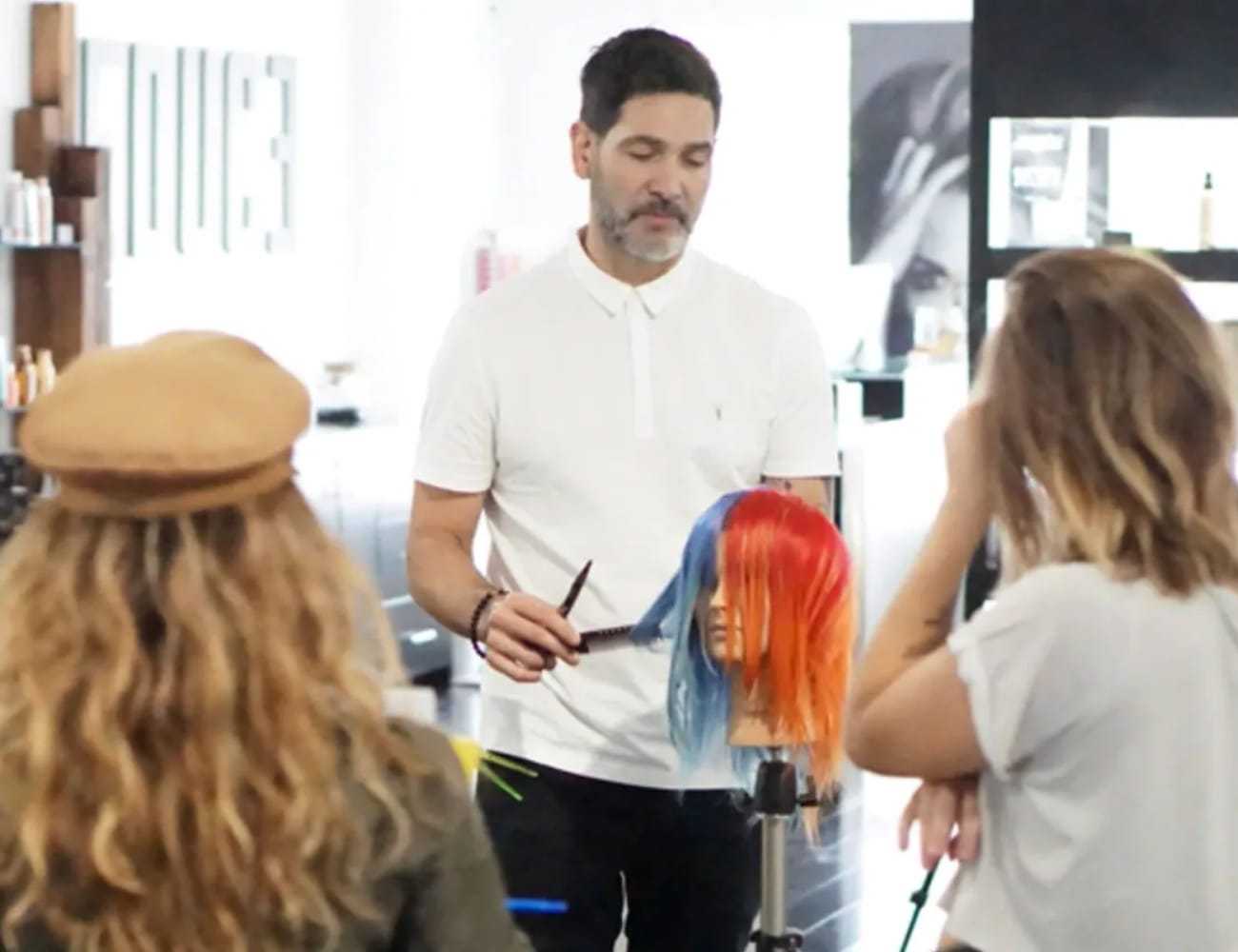 Man demonstrating hair coloring techniques on a mannequin to a group in a salon setting.