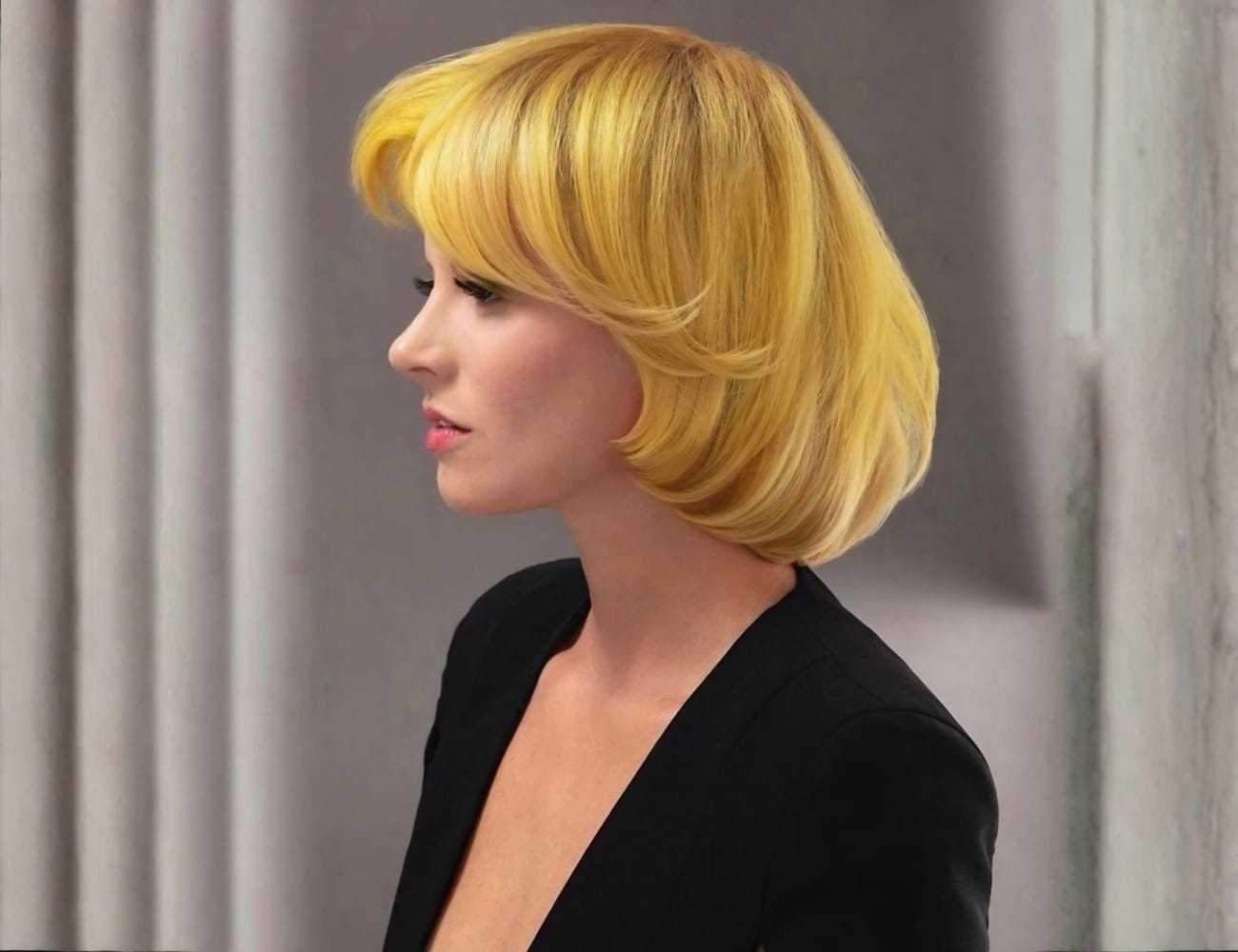 A woman with short blonde hair in profile, wearing a black outfit against a muted backdrop.