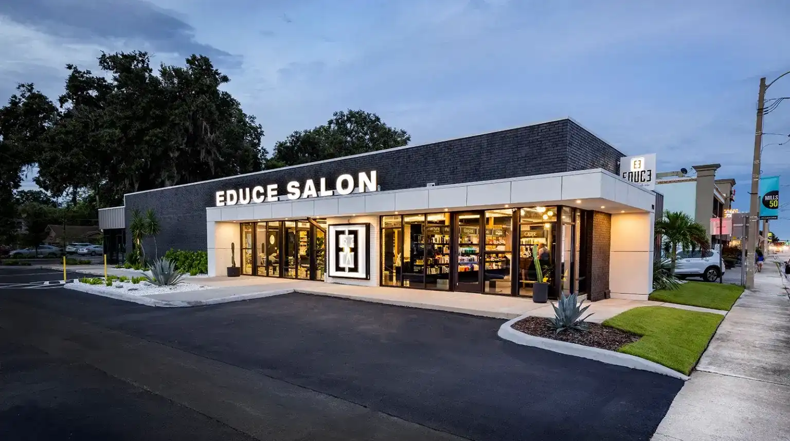 Modern hair salon exterior with large windows and lit sign in an urban setting.