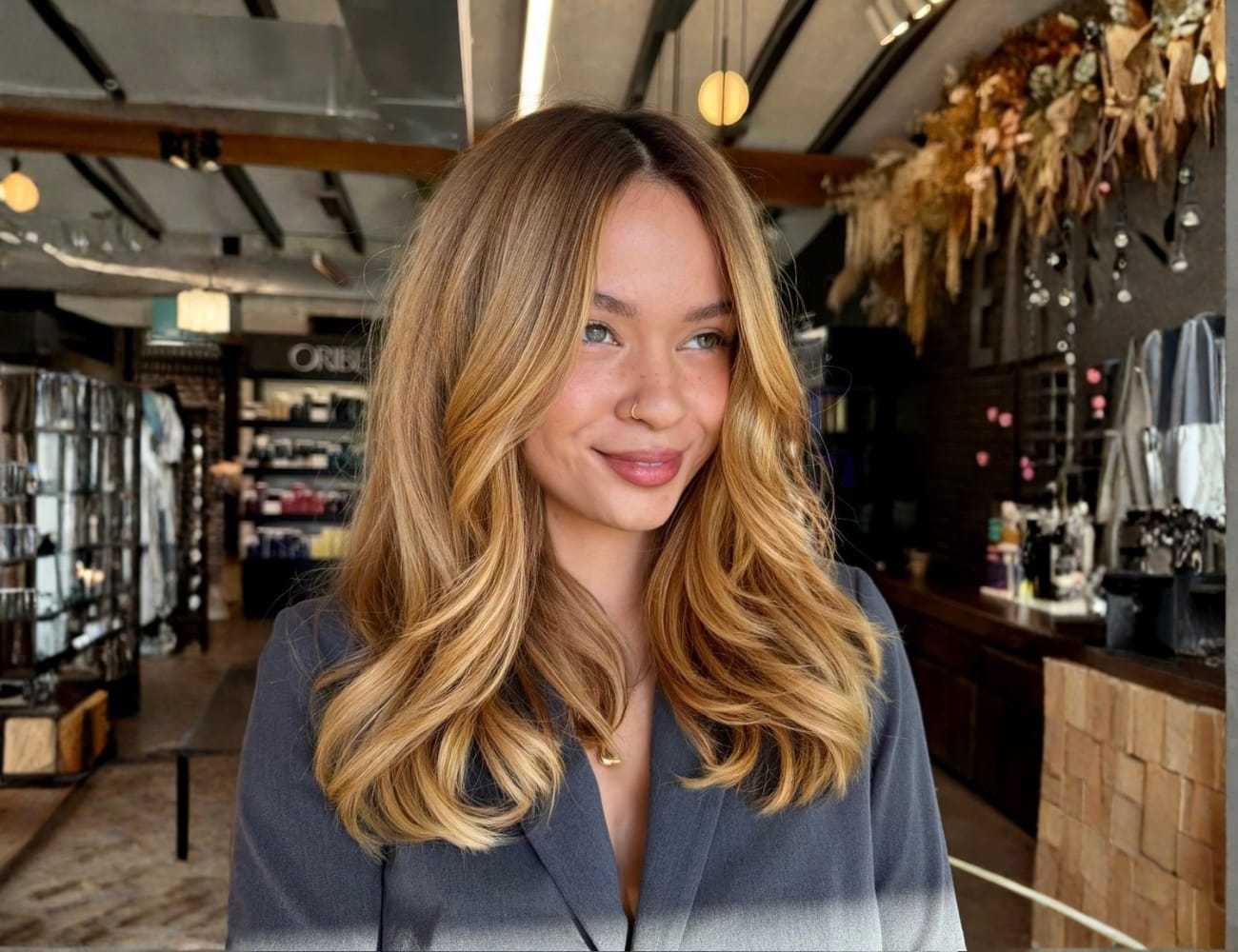 Young woman with long, wavy blonde hair, smiling in a stylish store setting.