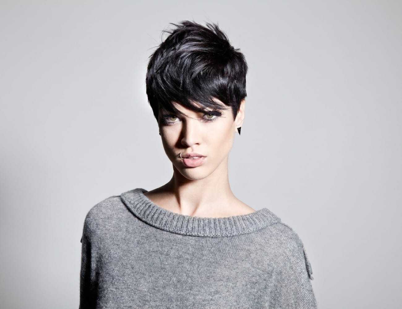 Short-haired person in a gray sweater with a neutral expression against a plain background.
