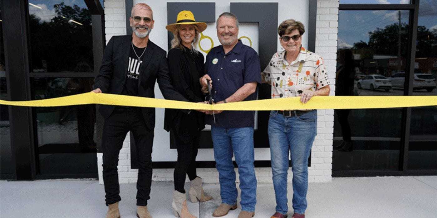 Four people celebrate a ribbon-cutting ceremony in front of a store.