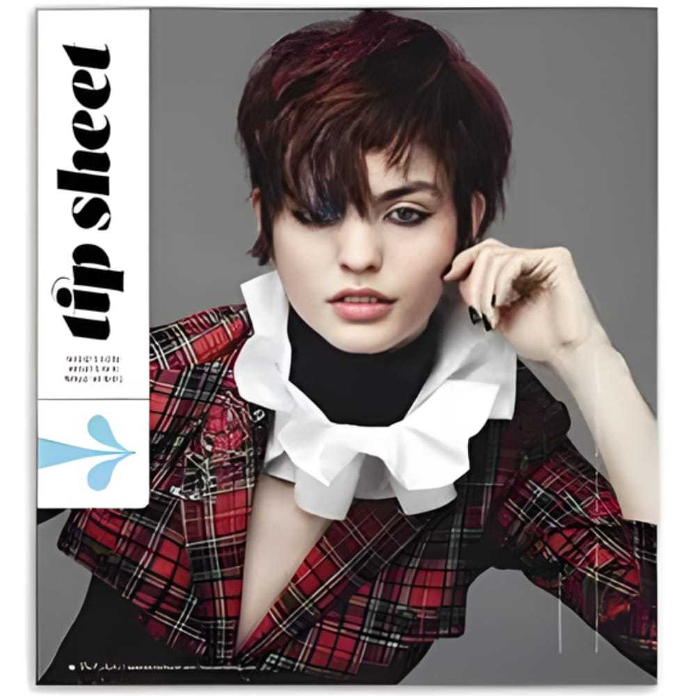 Short-haired model in red plaid outfit with large white collar, posing with hand near face.